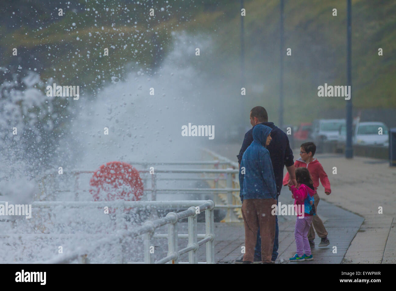 Aberystwyth, Wales, Regno Unito. Il 4 agosto 2015. Le tempeste. Un 5-8 piedi si gonfiano, venti alti e un alta marea cmbine per ancorare Aberystwyth lungomare con grandi onde. Una famiglia in vacanza gioca a schivare le onde sul lungomare Credito: Alan Hale/Alamy Live News Foto Stock
