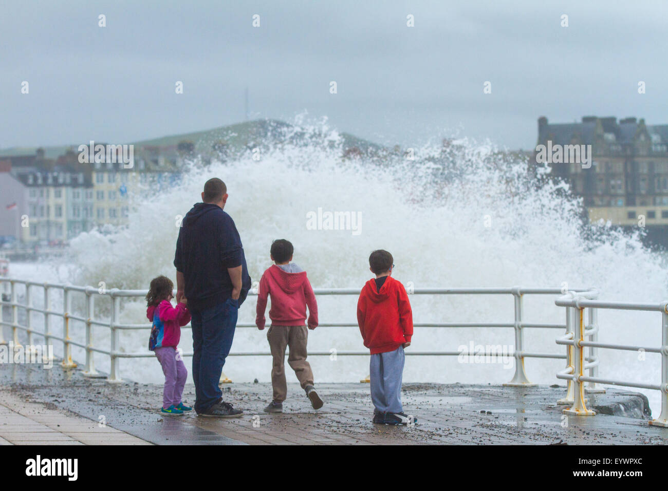 Aberystwyth, Wales, Regno Unito. Il 4 agosto 2015. Le tempeste. Un 5-8 piedi si gonfiano, venti alti e un alta marea cmbine per ancorare Aberystwyth lungomare con grandi onde. Una famiglia in vacanza gioca a schivare le onde sul lungomare Credito: Alan Hale/Alamy Live News Foto Stock