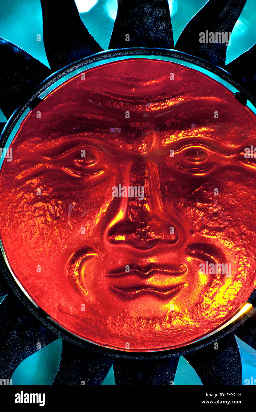 Vetro traslucido volto del Dio Sole scultura e raggi che si estende con una bassa impostazione rosso sole che illumina le sue funzioni Foto Stock