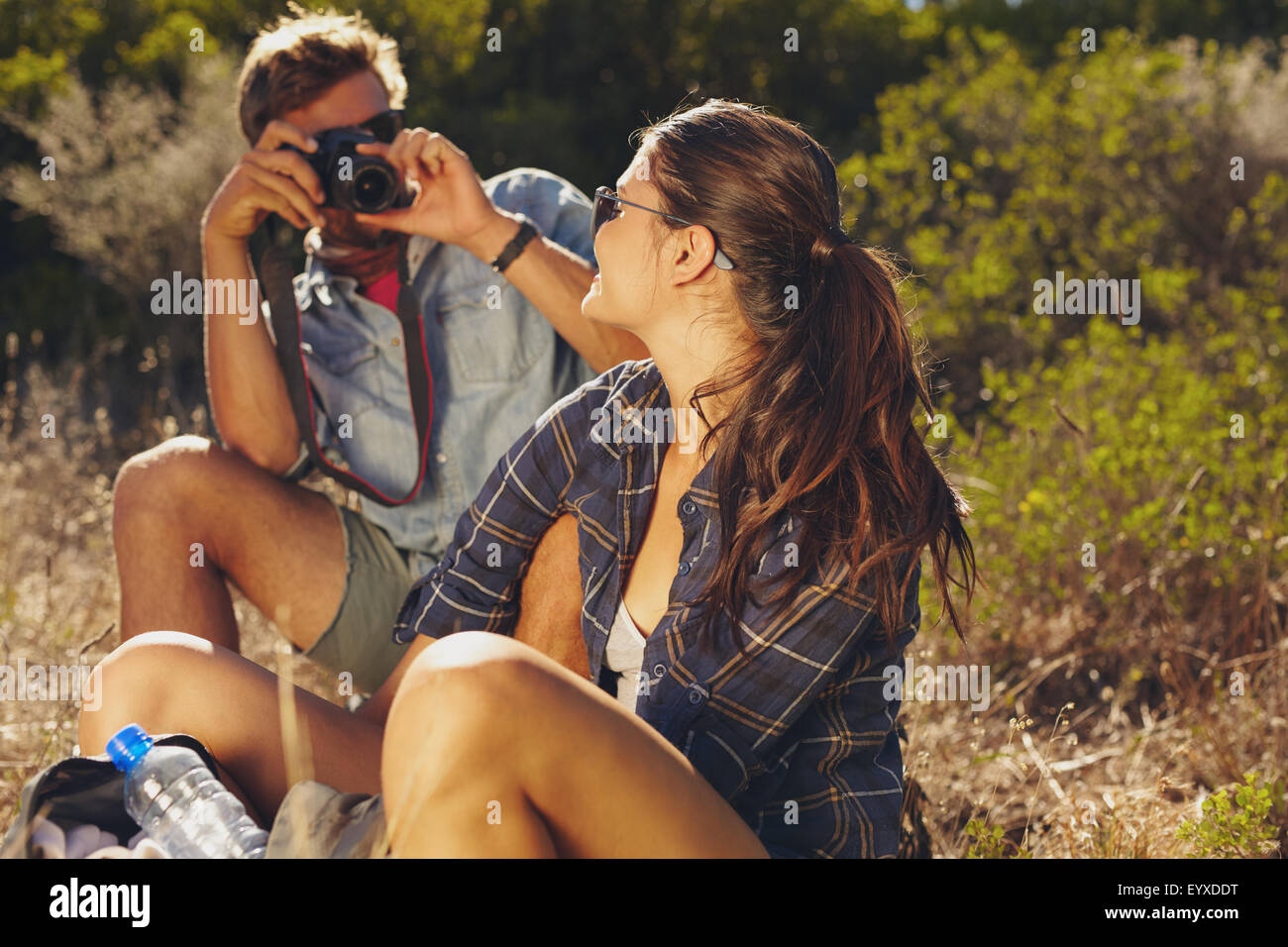 Giovane uomo di fotografare la sua fidanzata mentre si è in viaggio escursionistico. Giovane seduto e rilassante, prendendo una pausa. Foto Stock