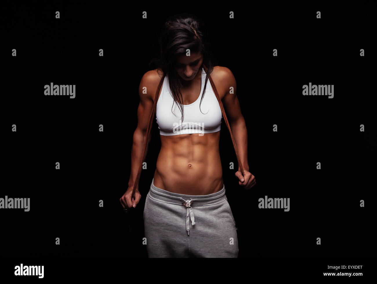 Ritratto di donna muscolare holding salto con la corda. Femmina modello di fitness con corda da salto su sfondo nero Foto Stock
