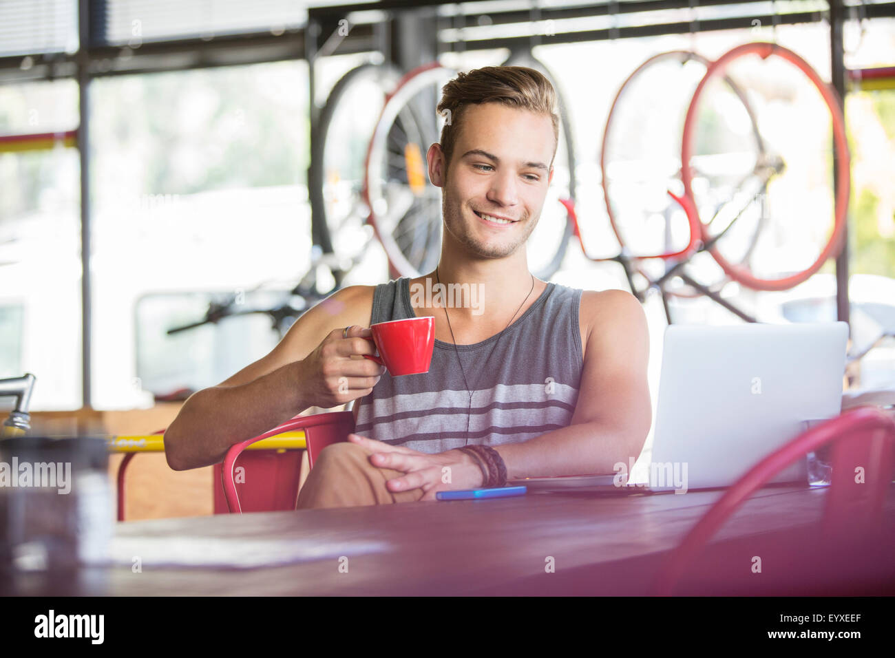 Uomo sorridente di bere il caffè al computer portatile in bike shop Foto Stock