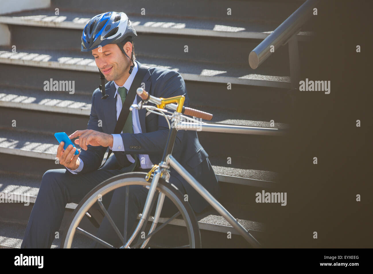 Imprenditore della tuta con bicicletta e casco texting con un telefono cellulare su scale Foto Stock Imprenditore della tuta con bicicletta e casco texting con un telefono cellulare su scale Foto Stock