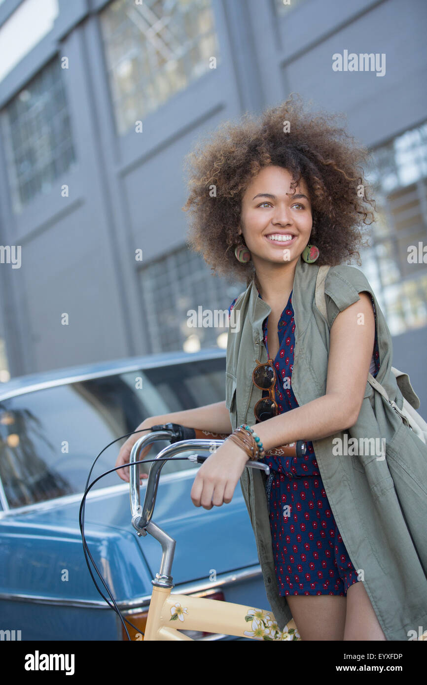 Sorridente giovane donna con afro holding bicicletta su strada urbana Foto Stock