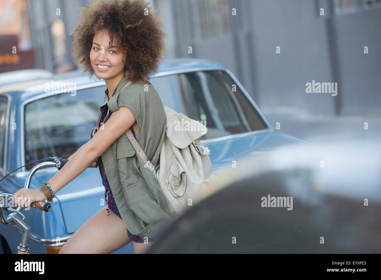 Ritratto di donna sorridente con afro sulla bicicletta in strada urbana Foto Stock