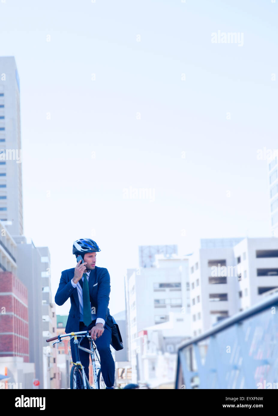 Imprenditore della tuta e casco parlando al cellulare in bicicletta in città Foto Stock