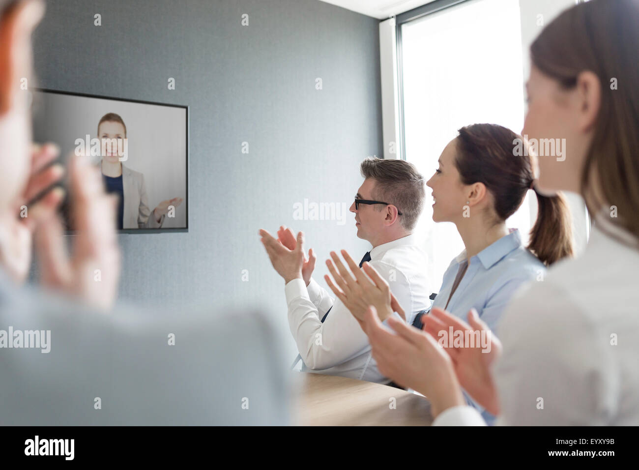 La gente di affari battimani per imprenditrice sul video nella schermata di conferenza Foto Stock