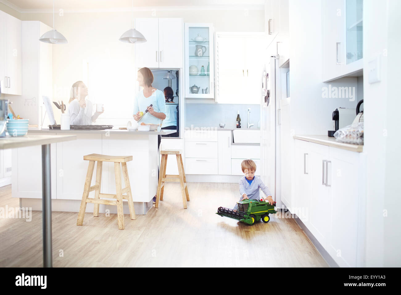 Le donne per la cottura in cucina mentre il ragazzo gioca con il trattore giocattolo sul pavimento Foto Stock