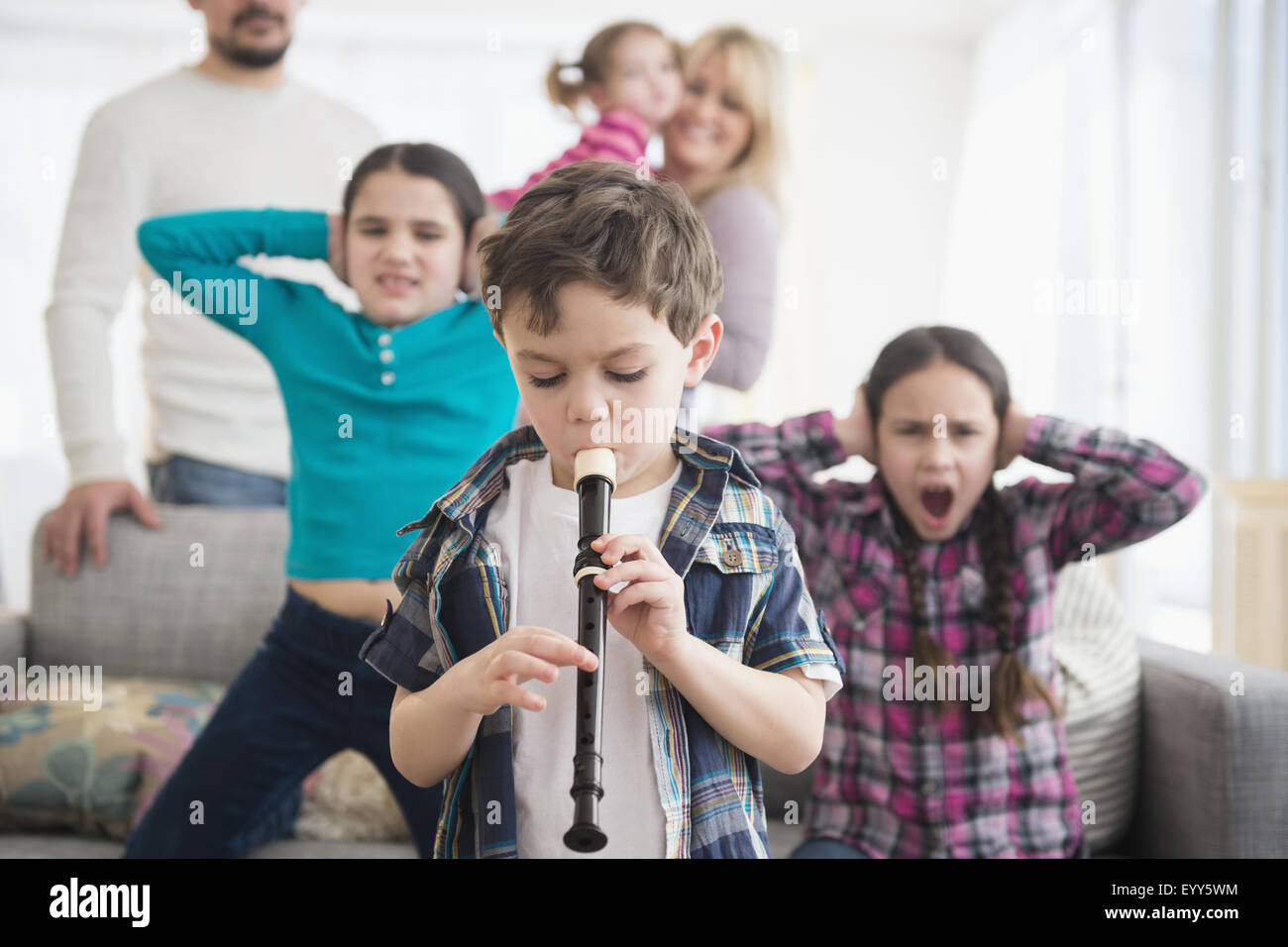 Famiglia caucasica che copre le orecchie con ragazzo giocando recorder Foto Stock