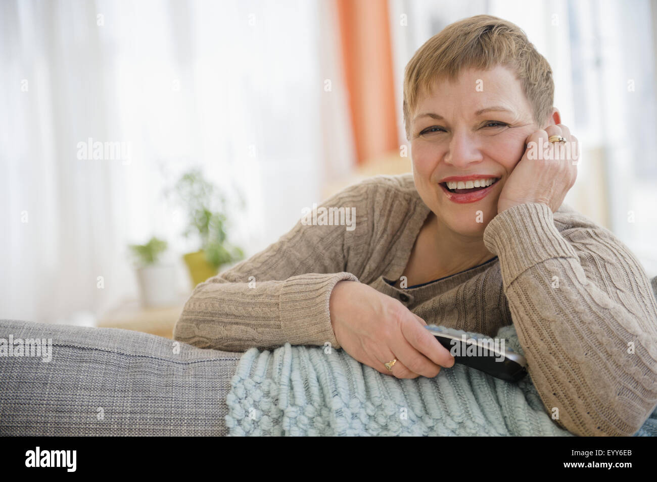 La donna caucasica tenendo premuto il telecomando sul divano Foto Stock