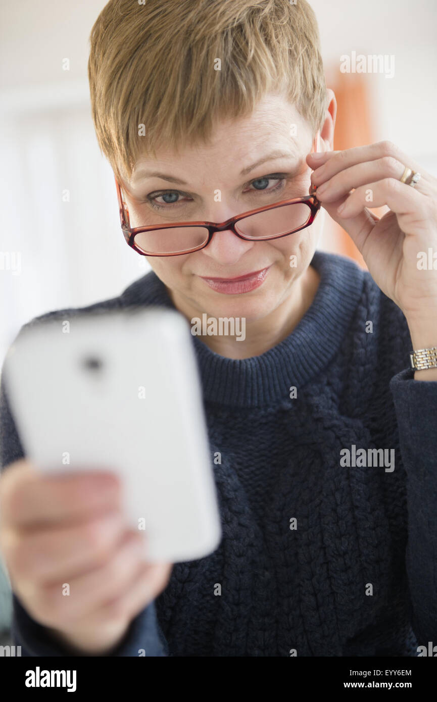 La donna Caucasica del peering sopra gli occhiali al telefono cellulare Foto Stock