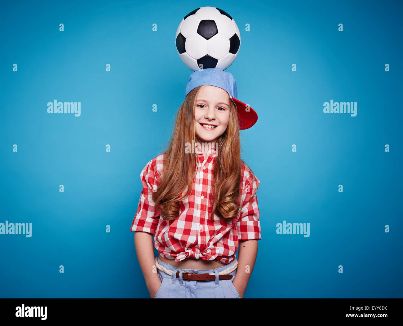 Ragazza sorridente guardando la fotocamera con pallone da calcio sulla sua testa Foto Stock