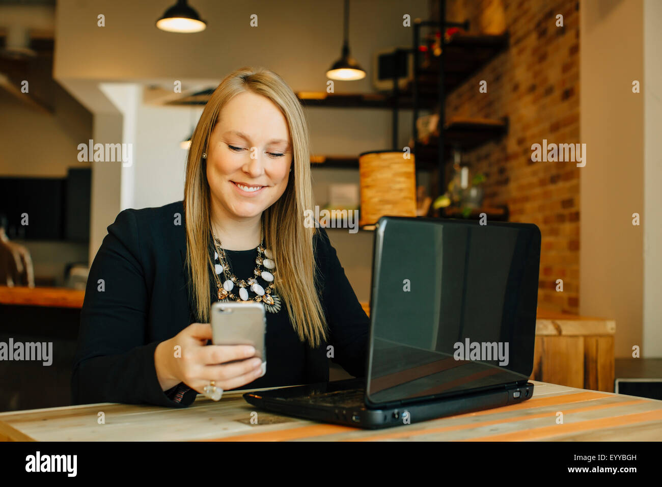 Imprenditrice caucasica utilizzando laptop e telefono cellulare in cafe Foto Stock