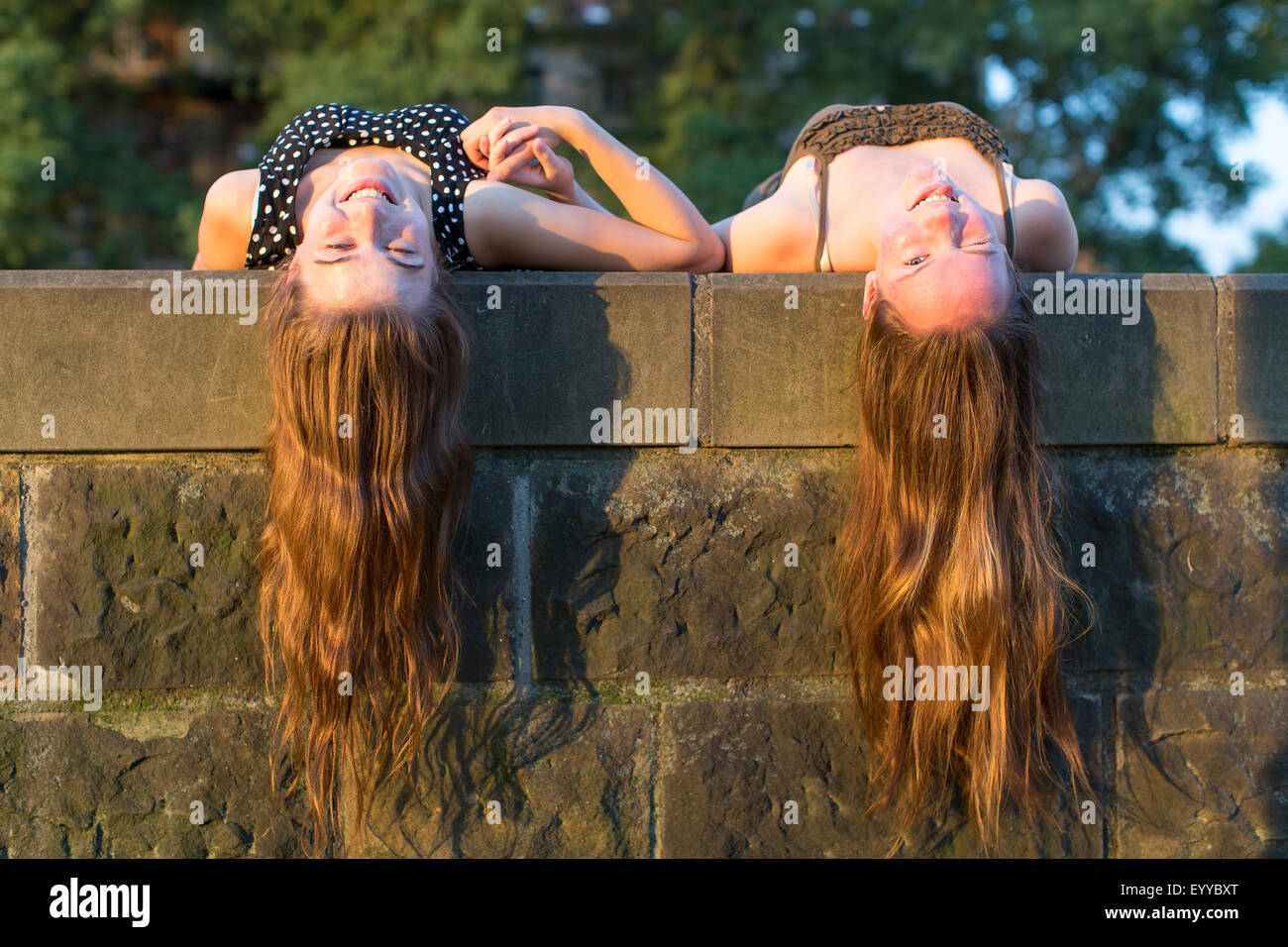 Due giovani ragazze giacente su una lastra di pietra con capelli lunghi a penzoloni. Bella morbida luce del tramonto. Foto Stock