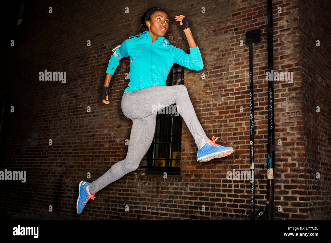 Nero donna salta vicino a un muro di mattoni di notte Foto Stock