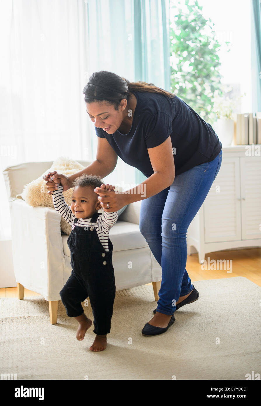 Razza mista madre aiutare baby figlio a piedi in salotto Foto Stock