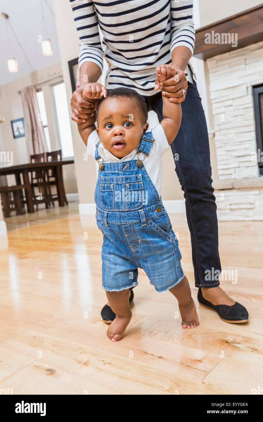 Madre nera aiutando baby figlio a piedi sul soggiorno piano Foto Stock