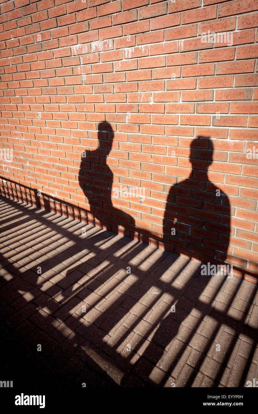 Le ombre di due persone sedute sul recinto contro un muro di mattoni. Foto Stock