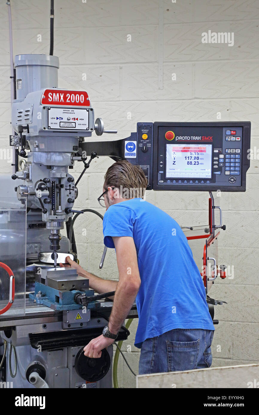 Un giovane lavoratore di sesso maschile crea un componente di acciaio utilizzando un moderno, informatizzato macchina perforatrice Foto Stock