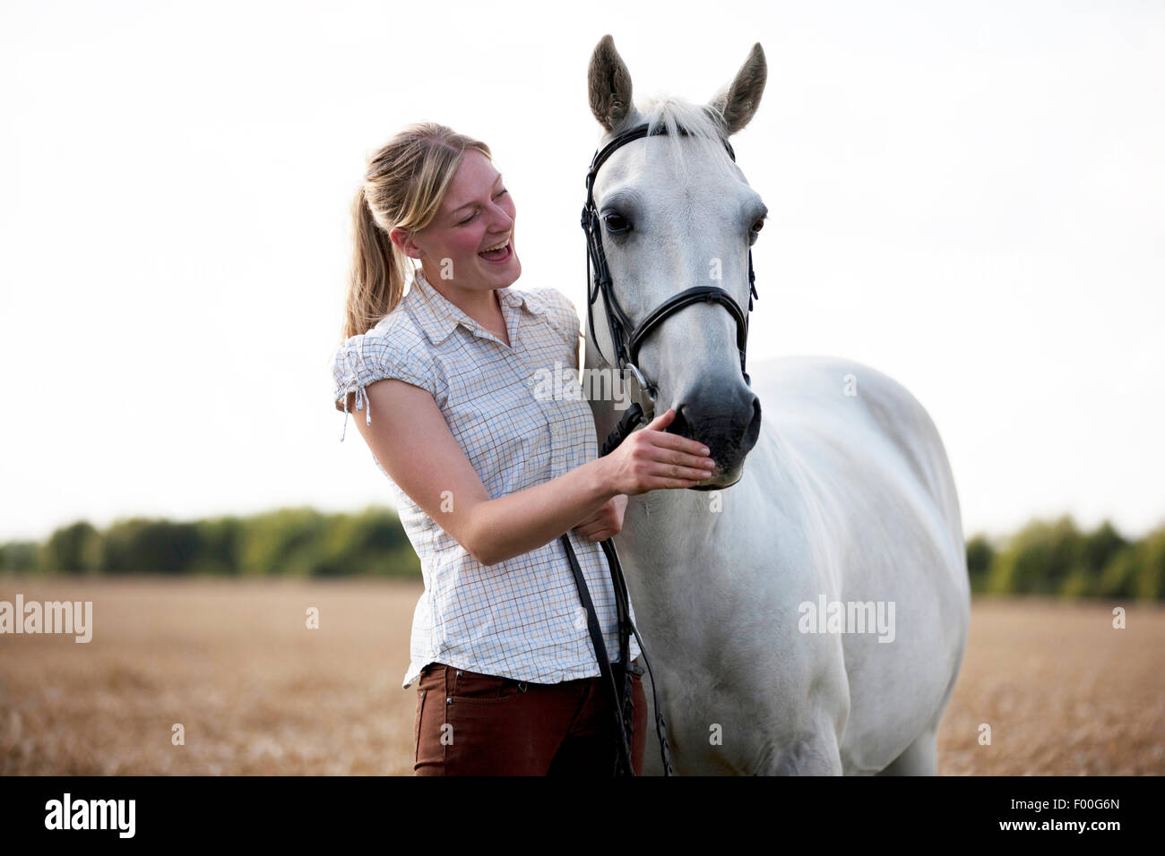 Una giovane donna in piedi in un campo di grano con un cavallo, ridendo Foto Stock