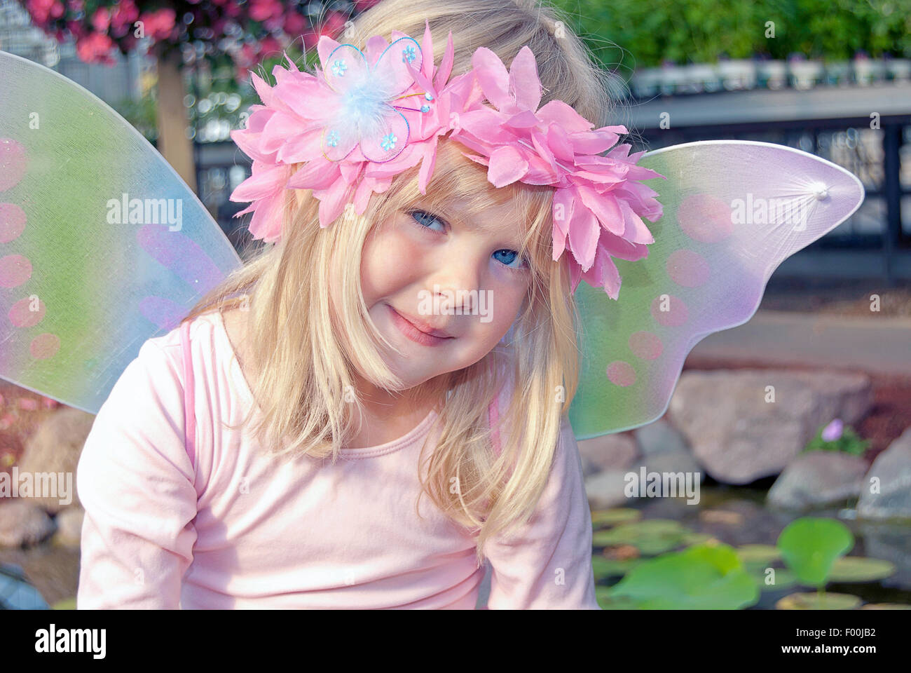 Sorridente bambina indossa un floreale alloro rosa nei capelli e ali di fata. Foto Stock