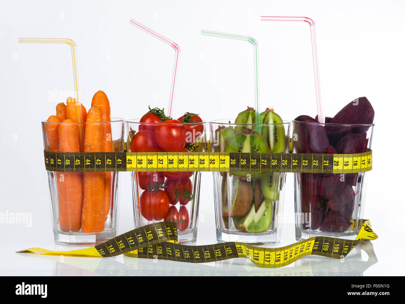 Immagine concettuale - La frutta e la verdura fresca in bicchieri di vetro con nastro di misurazione su uno sfondo bianco. Foto Stock