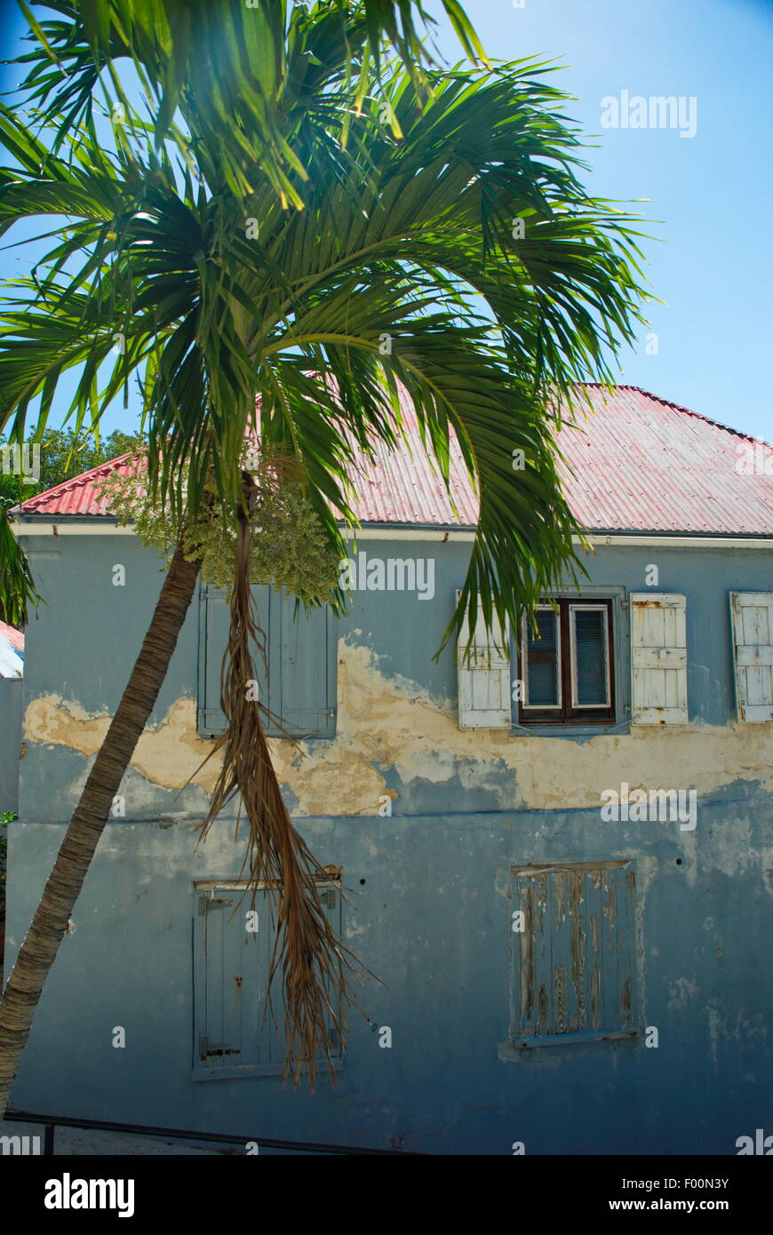 Lo stile caraibico architettura delle abitazioni, blu di età edificio con shuters, il tetto rosso e il palm tree sulla giornata di sole. Foto Stock