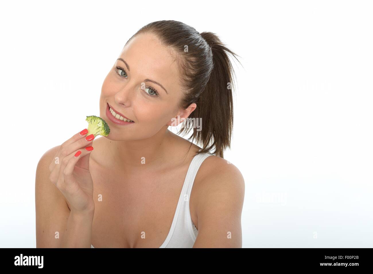 Felice positivo giovane donna mangiar sano non cotti crudo verdure broccoli isolata contro uno sfondo bianco con un tracciato di ritaglio Foto Stock