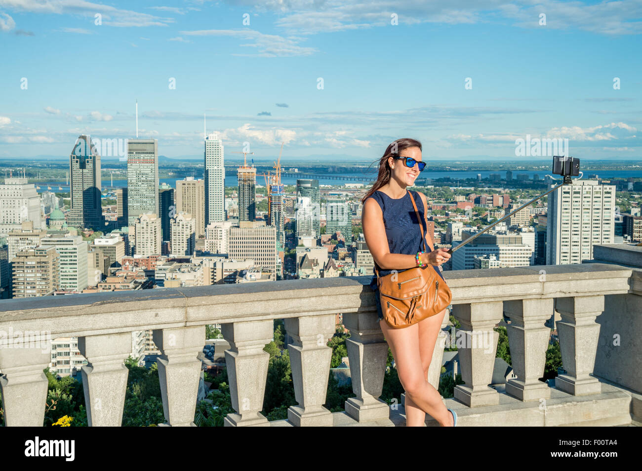 Giovane donna usando un bastone selfie nella parte anteriore della Skyline di Montreal, Kondiaronk belvedere. Foto Stock