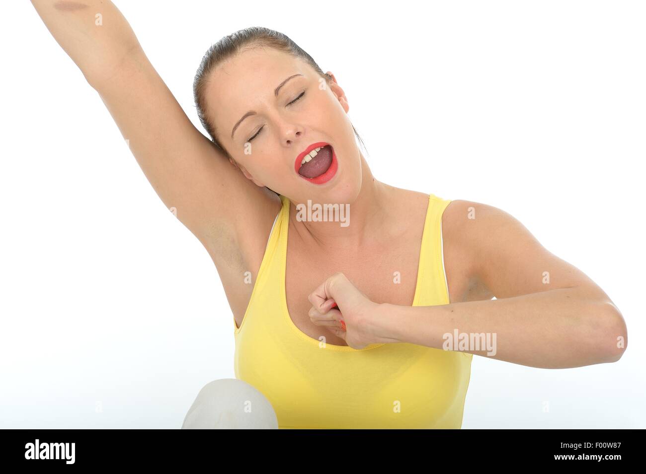 Attraente stanco esaurito giovane donna Stretching e sbadigli indossando un giallo brillante Vest alto isolato contro uno sfondo bianco con spazio di copia Foto Stock