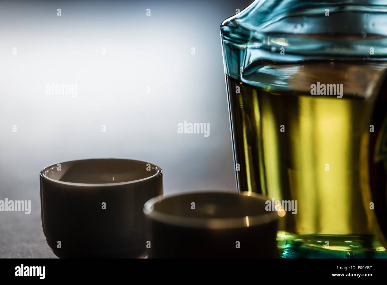 Una bottiglia del giapponese bere bene e per amor di ceramica tazze in controluce al buio su un tavolo di legno. Foto Stock