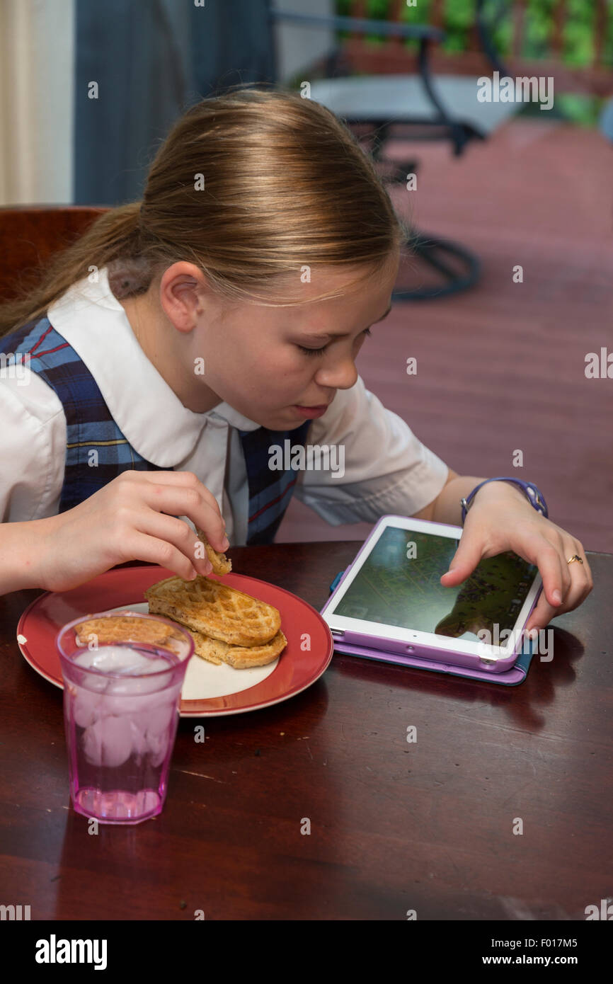 Ragazza giovane (undici anni) utilizzando l'iPad mentre si consuma la prima colazione. Signor Foto Stock