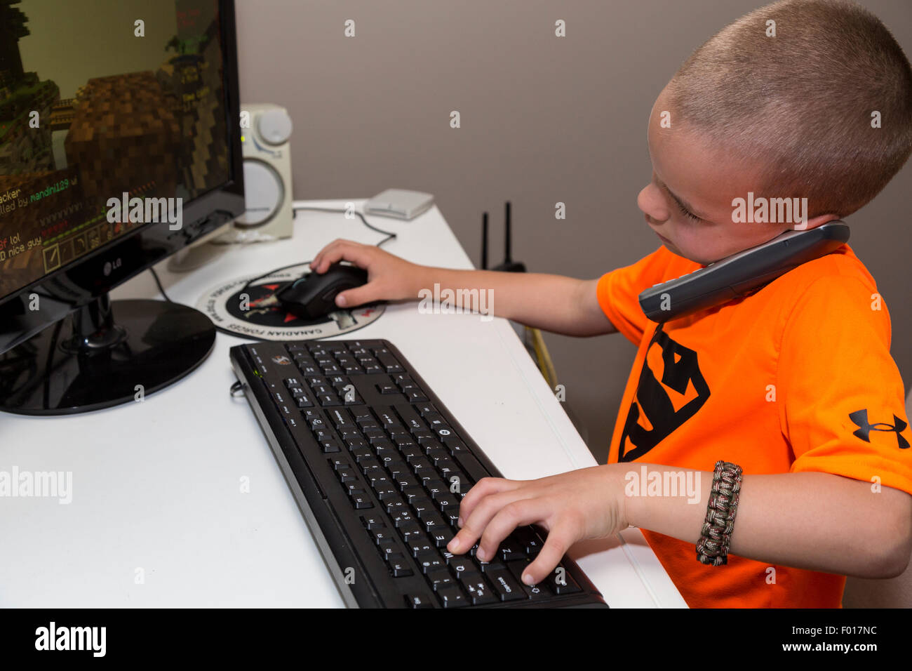 Il Multitasking inizia presto. Young Business Executive in formazione. Sette anni di vecchio ragazzo parla al telefono durante la riproduzione di video. Foto Stock