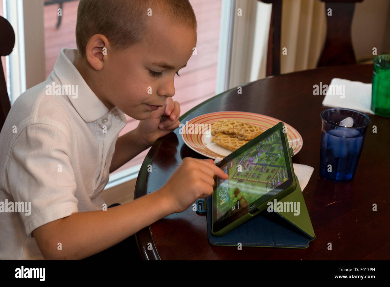 Giovane ragazzo (sette anni) giocando sul suo iPad mentre si consuma la prima colazione. Signor Foto Stock