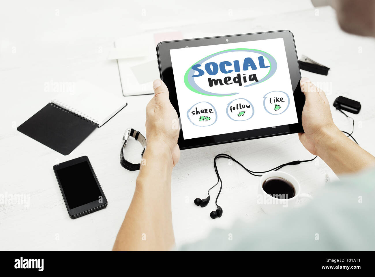 Uomo al lavoro su un tablet pc con i social media concetto sullo schermo, il blocco note e smart phone sul tavolo bianco. Foto Stock