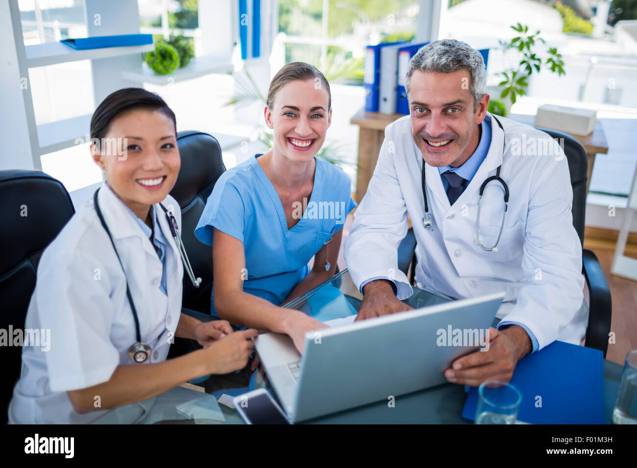 Medici e infermieri guardando laptop e sorridente in telecamera Foto Stock