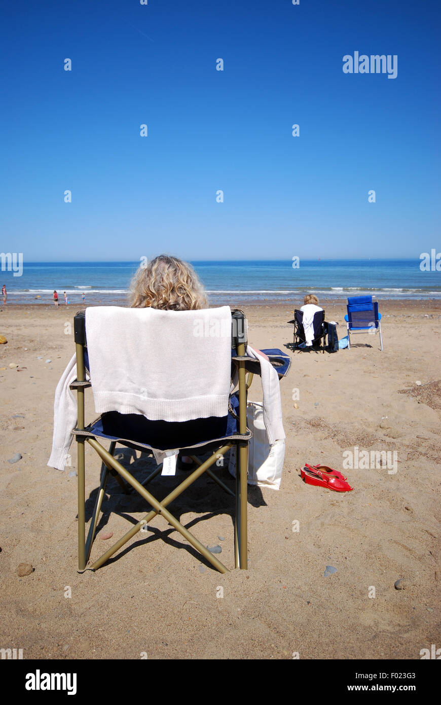 Donna seduta accanto al mare in una sedia su di una spiaggia di sabbia Foto  stock - Alamy