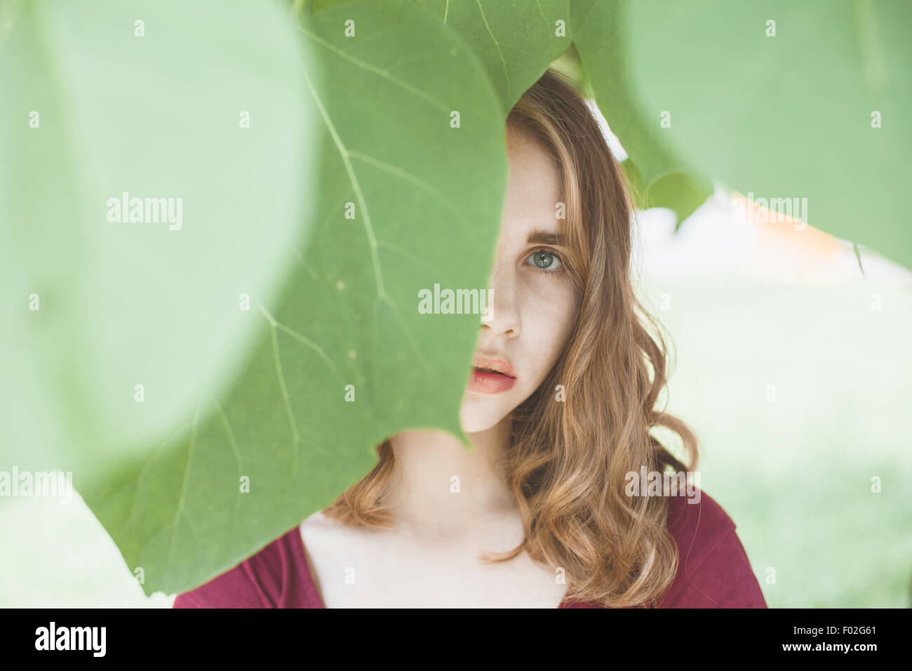 Ritratto di una giovane donna con la faccia oscurata da foglie Foto Stock
