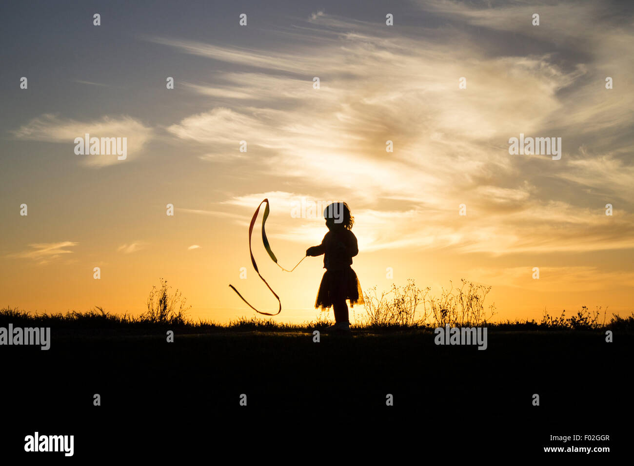 Silhouette di una ragazza che gioca con un nastro Foto Stock Silhouette di una ragazza che gioca con un nastro Foto Stock