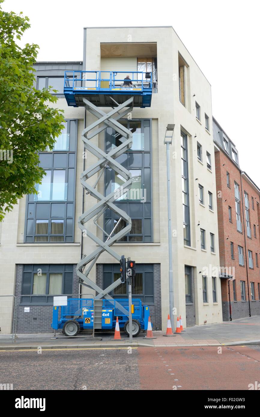 Un piccolo sistema idraulico di sollevamento a forbice piattaforma di lavoro accesso della superficie esterna di un edificio basso in Paisley, Renfrewshire, Scozia Foto Stock