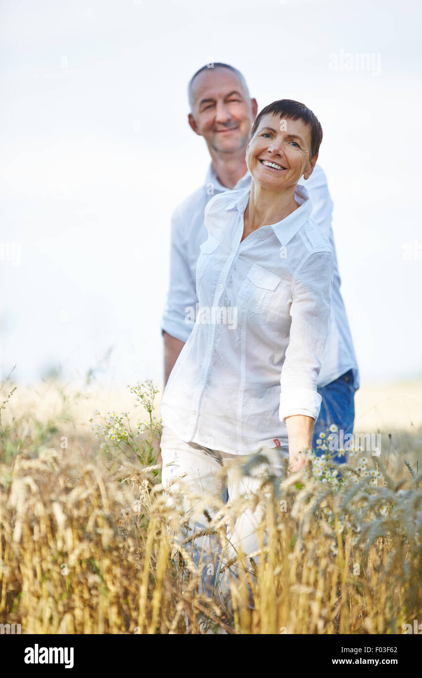 Felice coppia senior nel periodo delle vacanze estive a piedi attraverso un campo di grano Foto Stock