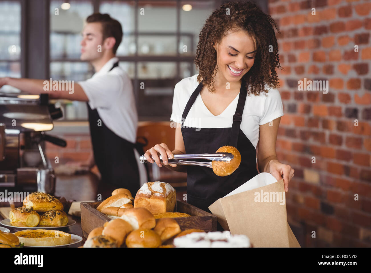 Sorridente cameriera mettendo panino nel sacchetto di carta Foto Stock