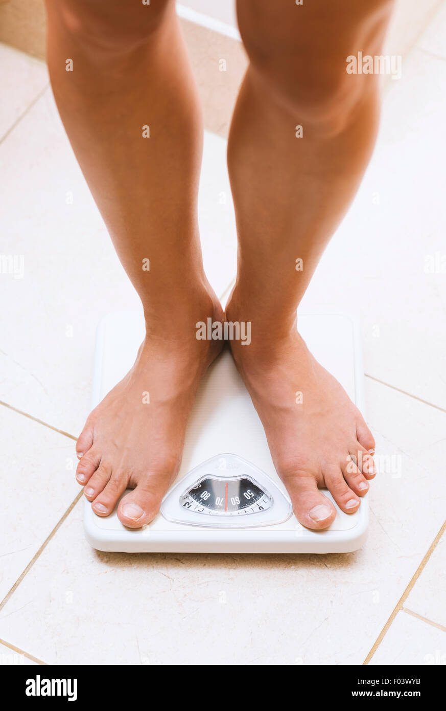 Donna di peso se stessa a piedi nudi sulla bilancia da bagno Foto Stock