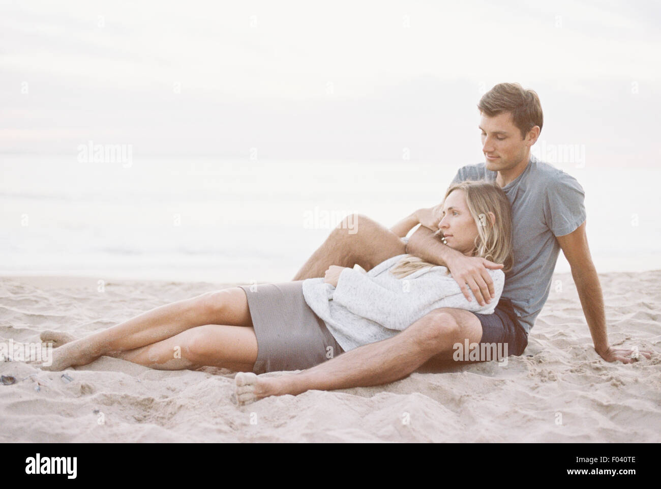 Un giovane seduto vicino a una spiaggia, un uomo e una donna con le braccia intorno a ogni altro e teste insieme. Foto Stock