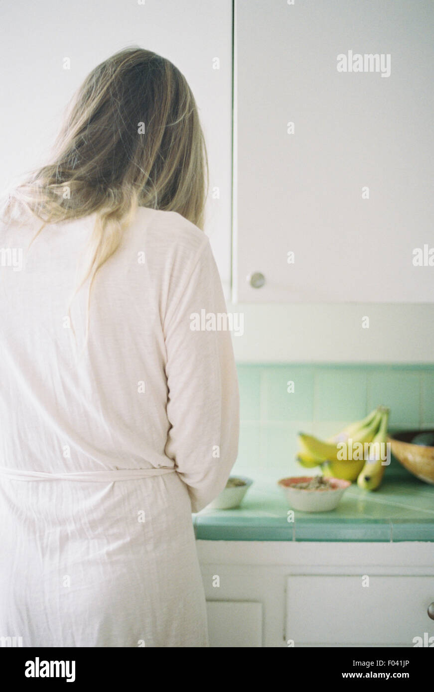 Vista posteriore di una donna in piedi in una cucina, preparare la prima colazione. Foto Stock