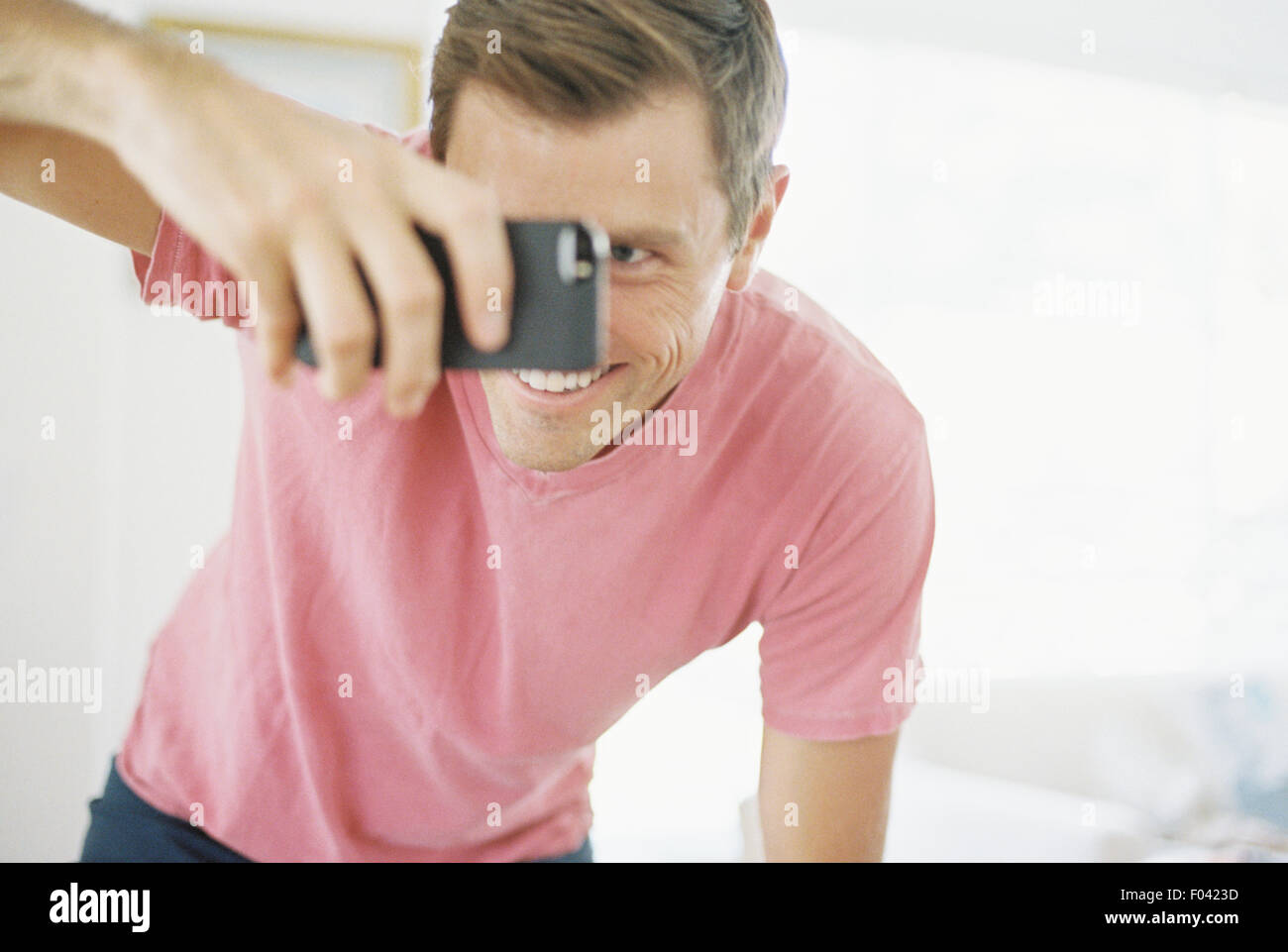 Uomo sorridente di scattare una foto con un telefono intelligente. Foto Stock