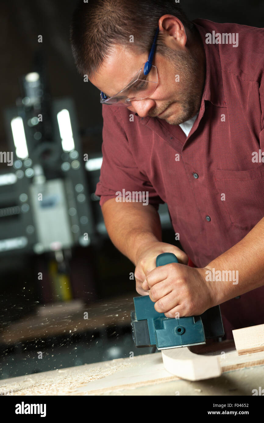 Carpenter lavora con pialla elettrica sul tavolato in legno in officina. Foto Stock