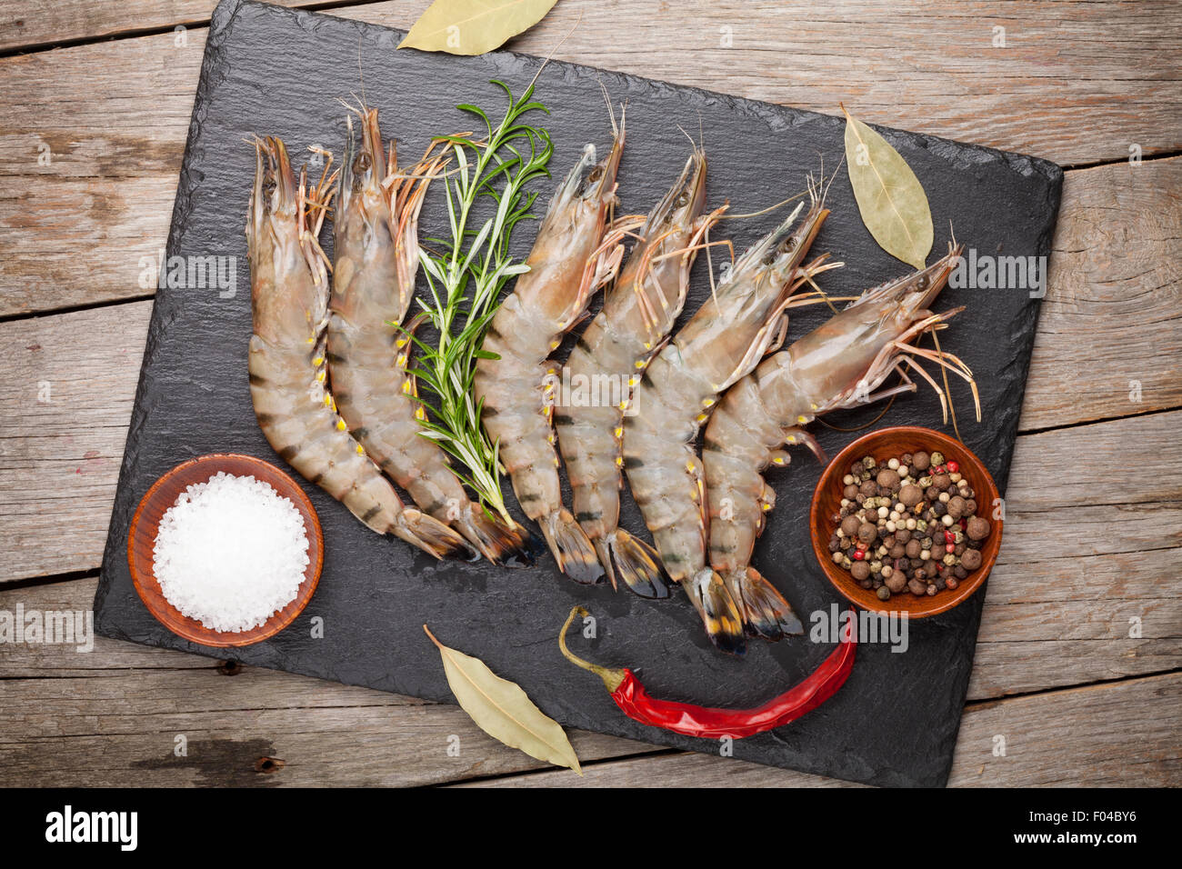 Crudo fresco gamberoni e spezie su pietra nera piastra sul tavolo di legno Foto Stock