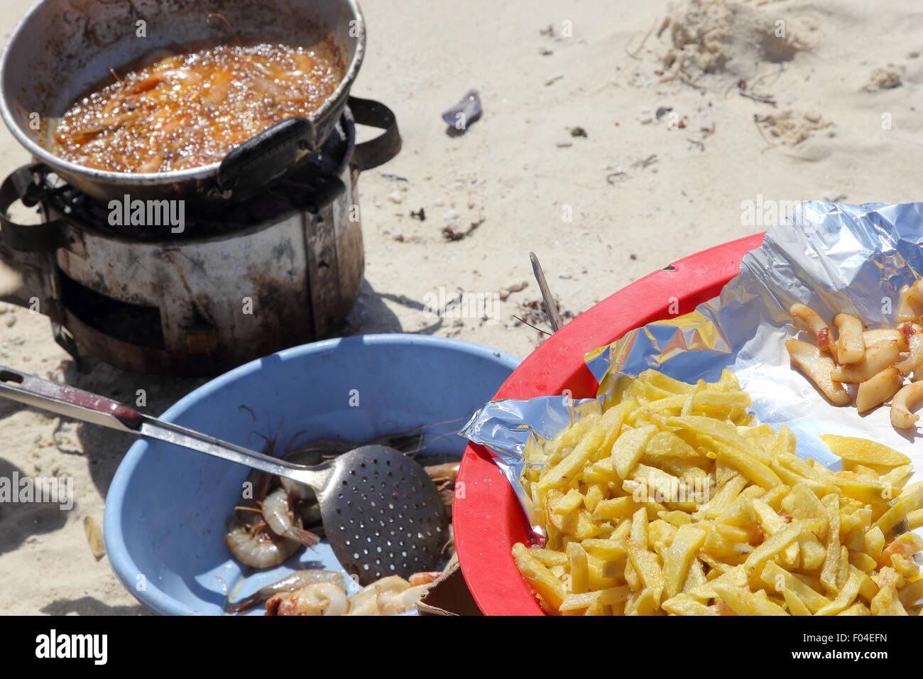 Una padella di olio caldo con gamberetti frittura sulla spiaggia con le patatine fritte come accompagnamento Foto Stock