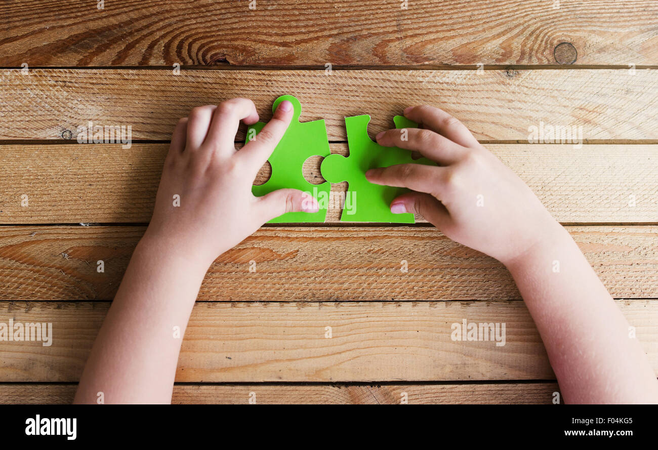 Immagine ritagliata delle mani di collegamento di due pezzi di un puzzle sul tavolo di legno Foto Stock